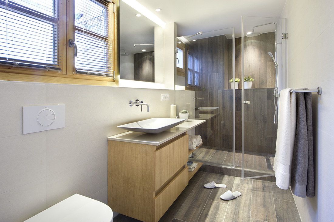 一个土色的浴室位于卧室的正内部。它有漂亮的木板地板，一个水槽，抽水马桶和一个带玻璃门的淋浴区。