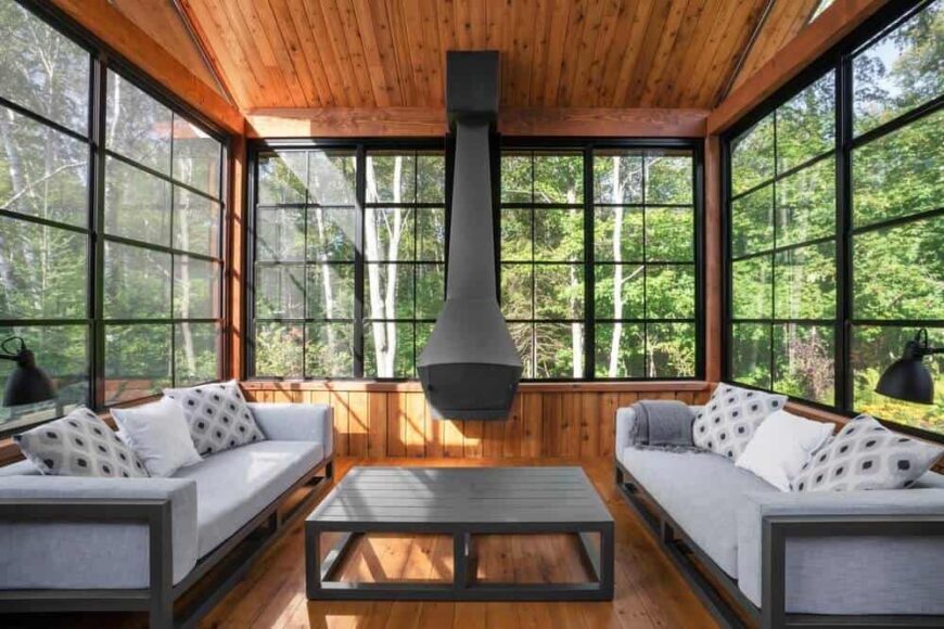 这间客厅以灰色沙发为特色，中间有一张方桌。它也有硬木地板和窗户，可以看到森林的美景。