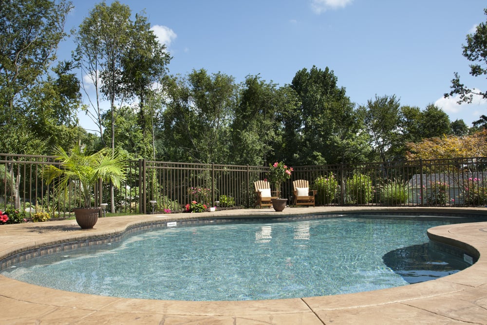 这是一个漂亮的肾形游泳池，浅棕色的石板露台，有一个环绕的安全围栏。