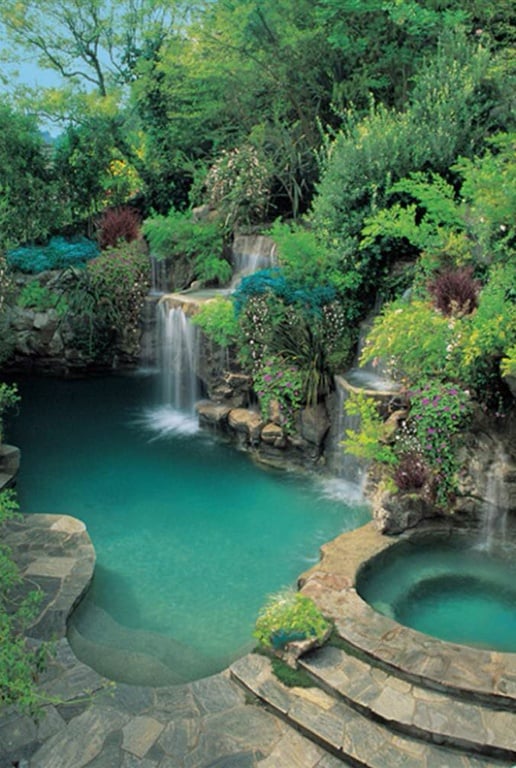 豪华自由肾形游泳池与瀑布和热水浴缸。这个游泳池周围的树木、灌木丛和鲜花使其更加壮观，它们向上梯田，形成了一个私人游泳绿洲。