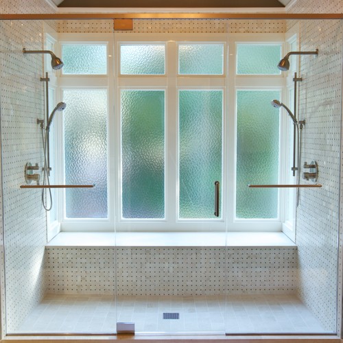 这间过渡浴室有迷你大理石瓷砖、一条长凳和两个淋浴头，位于一个封闭的空间内。/图片来源:Addhouse