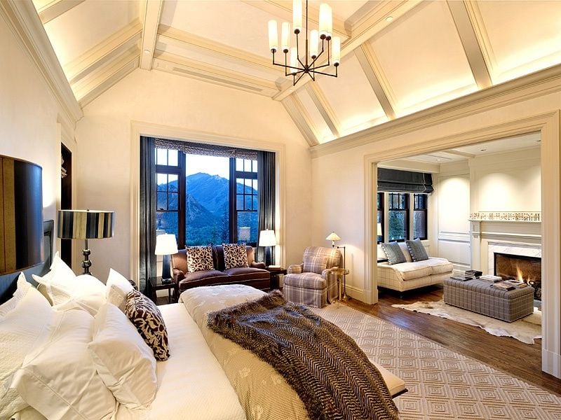 一间优雅的主卧室，带独立的起居空间和壁炉。房间的特色是米黄色的墙壁和硬木地板。