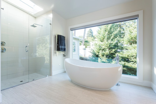 这间现代浴室有一个独立的浴缸，封闭的玻璃板淋浴和巨大的墙壁大小的窗户。/图片来源:JMJ工作室