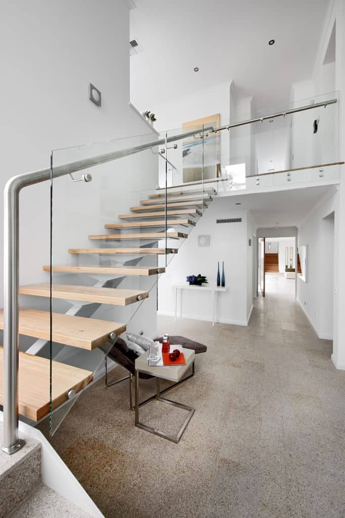 一个现代化的门厅提供一个休闲座椅和一个边桌就在楼梯下。楼梯以硬木台阶为特色，与玻璃栏杆很好地搭配。