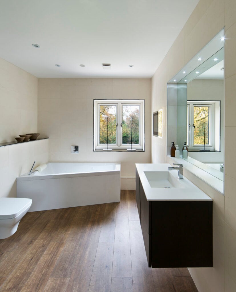 主浴室设有一个时尚的角落浴缸，设置在硬木地板上，周围是白色的墙壁和天花板。