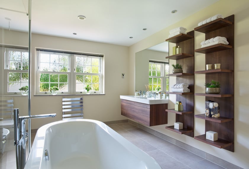 宽敞的主浴室设有一个白色的独立浴缸，几个架子和一个浮动的梳妆台。