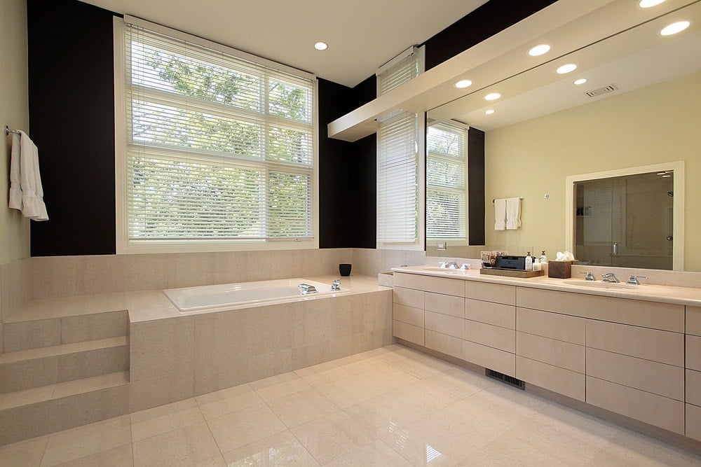 主浴室以瓷砖包裹的浸泡浴缸为特色，台阶从地板向上延伸。屋内的木质橱柜与瓷砖的米色相同，包括两个嵌入式水槽、一面镜子和充足的储物空间。照明由嵌入式灯具和大窗户提供。