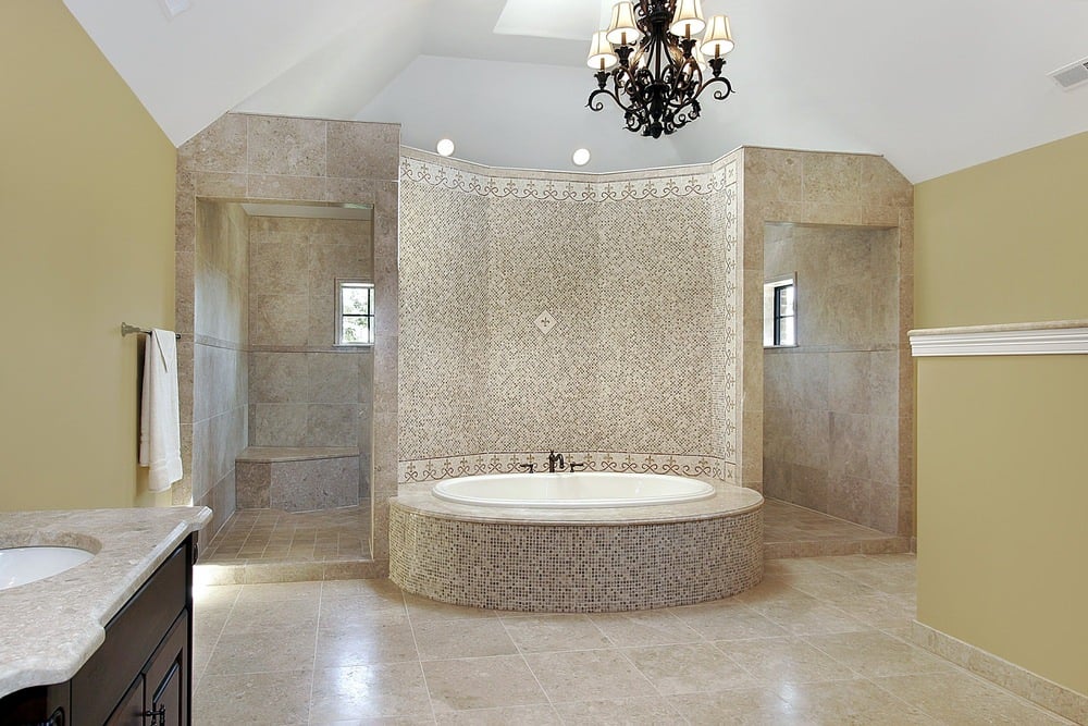 主浴室设有一个浸入式浴缸，带有通高的马赛克墙，将空间与带有瓷砖地板和墙壁的步入式淋浴间隔开。一盏黑色的枝形吊灯悬挂在高高的天花板上。