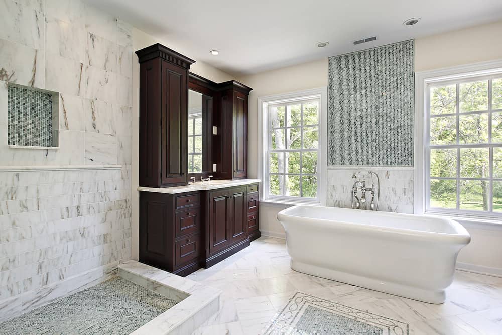 主浴室在设计上向经典的罗马建筑风格致敬，设有开放式的马赛克瓷砖浴室和大理石马赛克瓷砖地板上的独立浴缸。角落里有一个深色的木质梳妆台，旁边是浴缸和一组提供自然光的窗户。