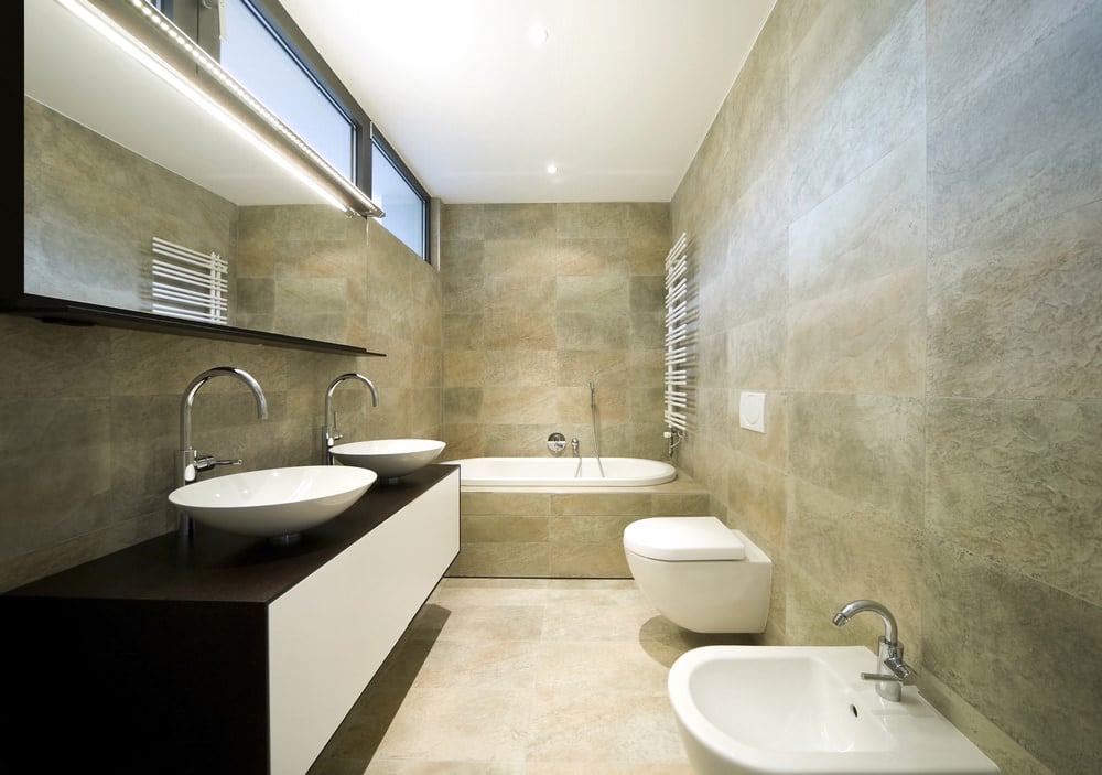 一间主浴室，在一个时尚的浮式梳妆台上提供一个角落的浴缸和几个水槽，周围环绕着优雅的瓷砖墙。