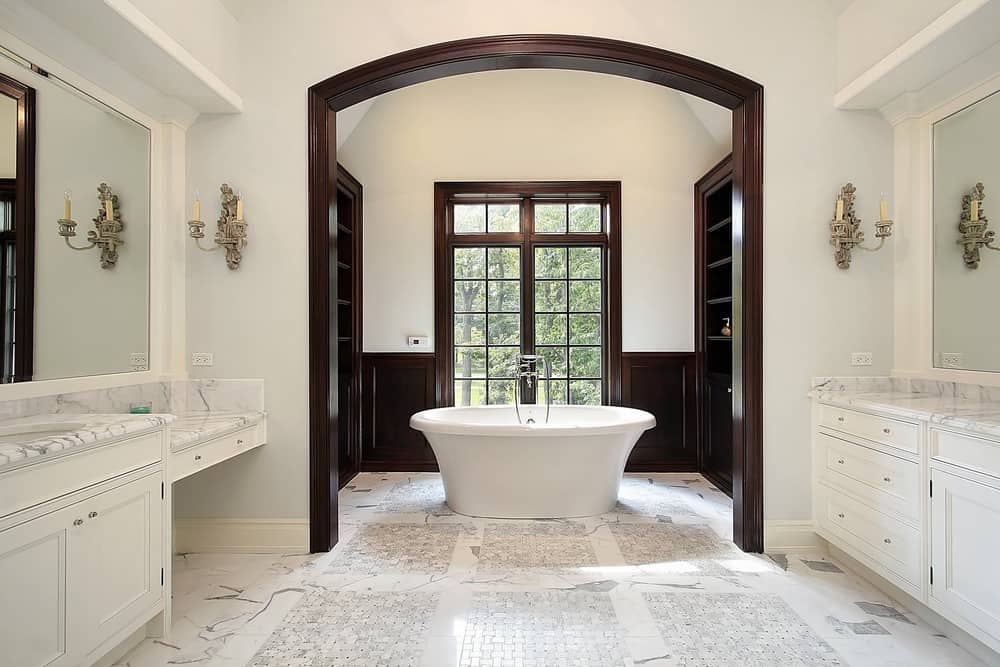 主浴室设有一个圆形的独立浴缸，设置在瓷砖地板上。房间里还有大理石台面的白色梳妆台，与凹室里的深色木质装饰和橱柜形成对比。