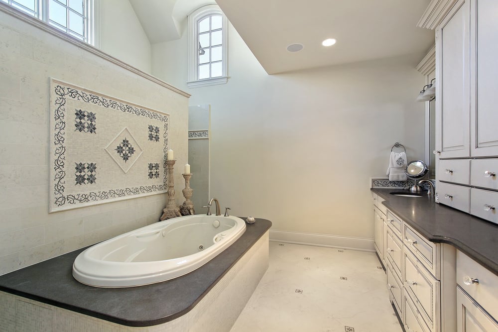 主浴室设有双层高的天花板，拱形天窗和部分墙壁，作为浸入式浴缸的空间分隔。这个空间包括白色橱柜和白色大理石瓷砖地板，台面和浴缸周围有深灰色大理石。