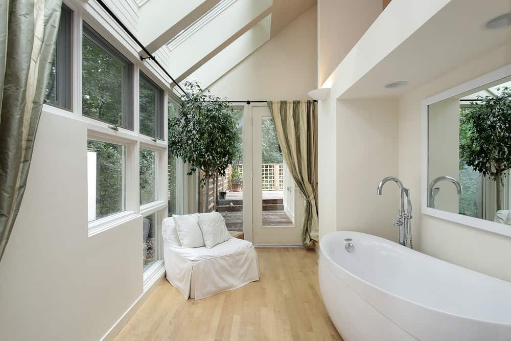 小型主浴室设有一个大型独立浴缸和硬木地板上的白色椅子。房间的拱形天花板也有天窗。