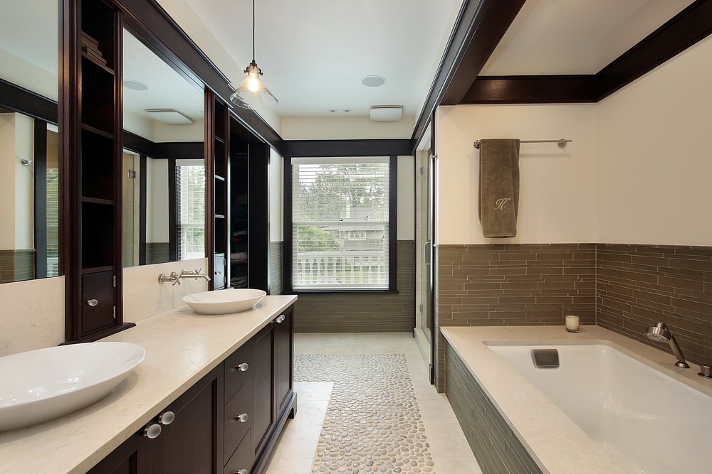 这间浴室里有一个固定在地铁瓷砖后挡板上的浴缸，还有一个深色木质双容器洗手台，上面有磨砂玻璃旋钮，镜子之间有内置搁板。