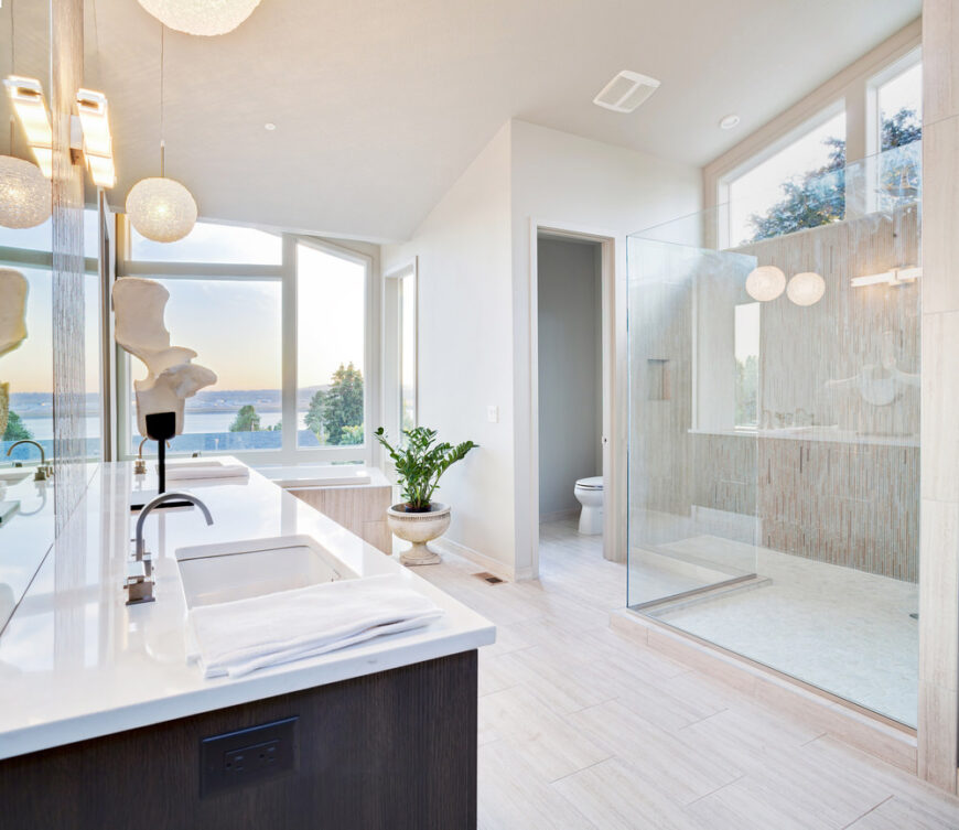 白色主浴室带有一个双水槽、一个步入式淋浴间和一个靠近窗户的浴缸，可以俯瞰令人放松的室外景色。
