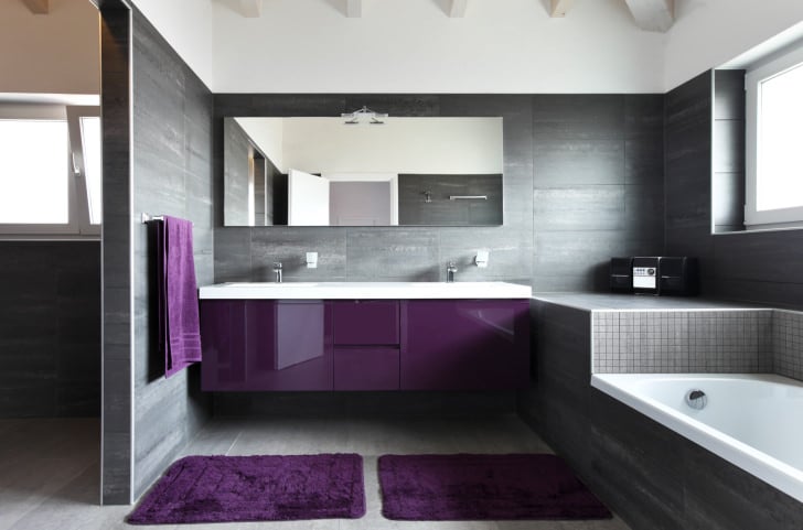 当代的主浴室，灰色的墙壁和地板以及紫色的阴影。该房间设有一个可入式浴缸和一个带有浮动梳妆台的双水槽。