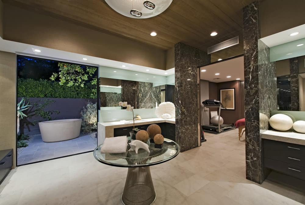 现代化的主浴室，带有室外独立浴缸和玻璃餐桌，以及一个小的健身房区域。
