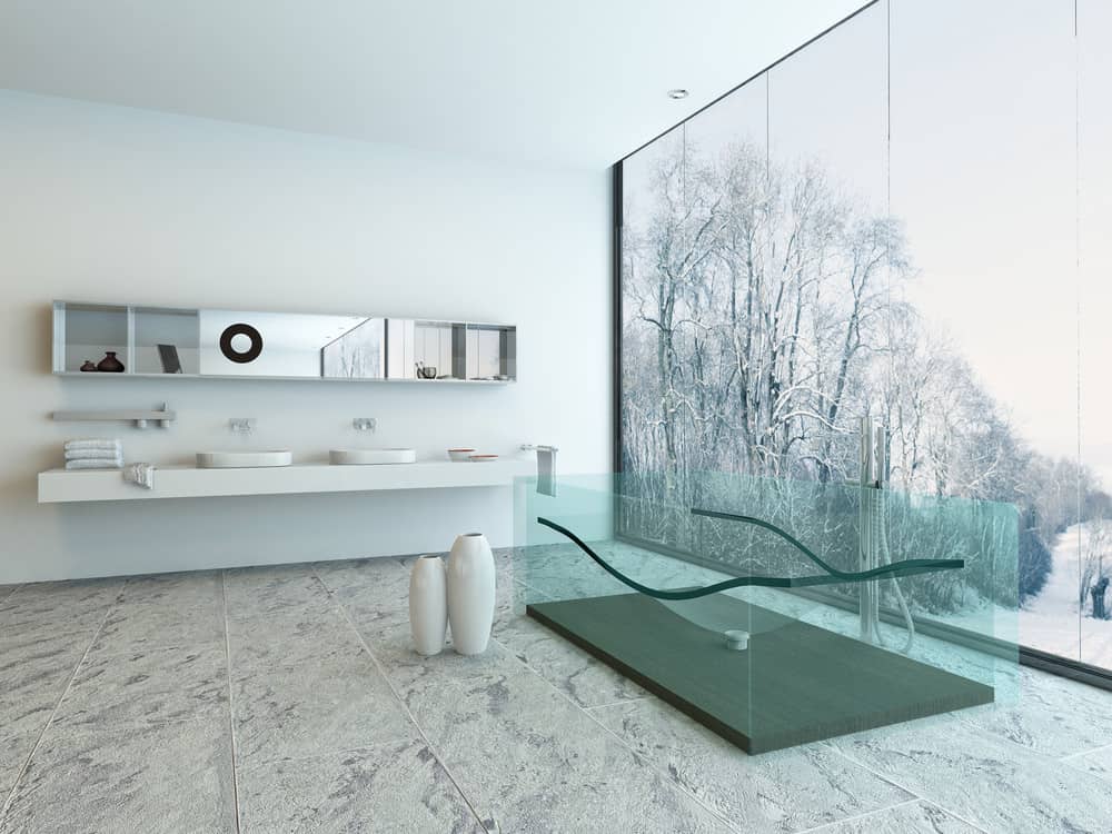 当代风格的主浴室以瓷砖地板为特色，带有容器水槽的浮动梳妆台和透明的独立浴缸，框架内设计了符合人体工程学的身体模具。