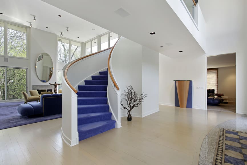 一座现代的房子，有漂亮的弧形楼梯，蓝色地毯地板和木制扶手。