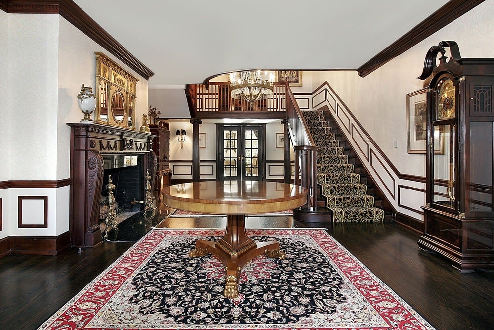经典的门厅设有一个圆形的木制中心桌子，坐在红色的复古地毯上，深色的木制楼梯穿着优雅的黑色楼梯。