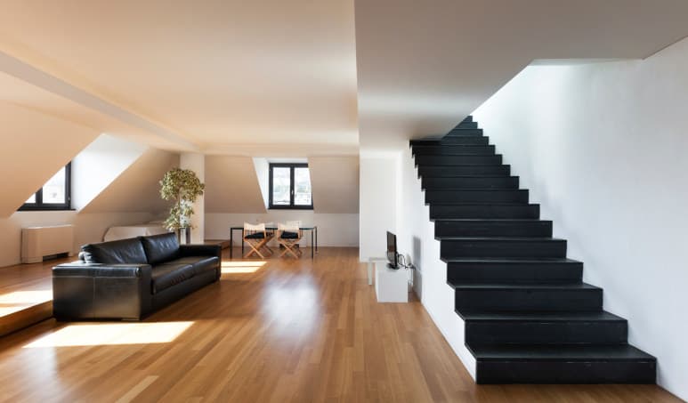 宽敞的客厅设有拱形墙壁和硬木地板，以及黑色沙发，与固定在白墙上的直楼梯相辅相成。