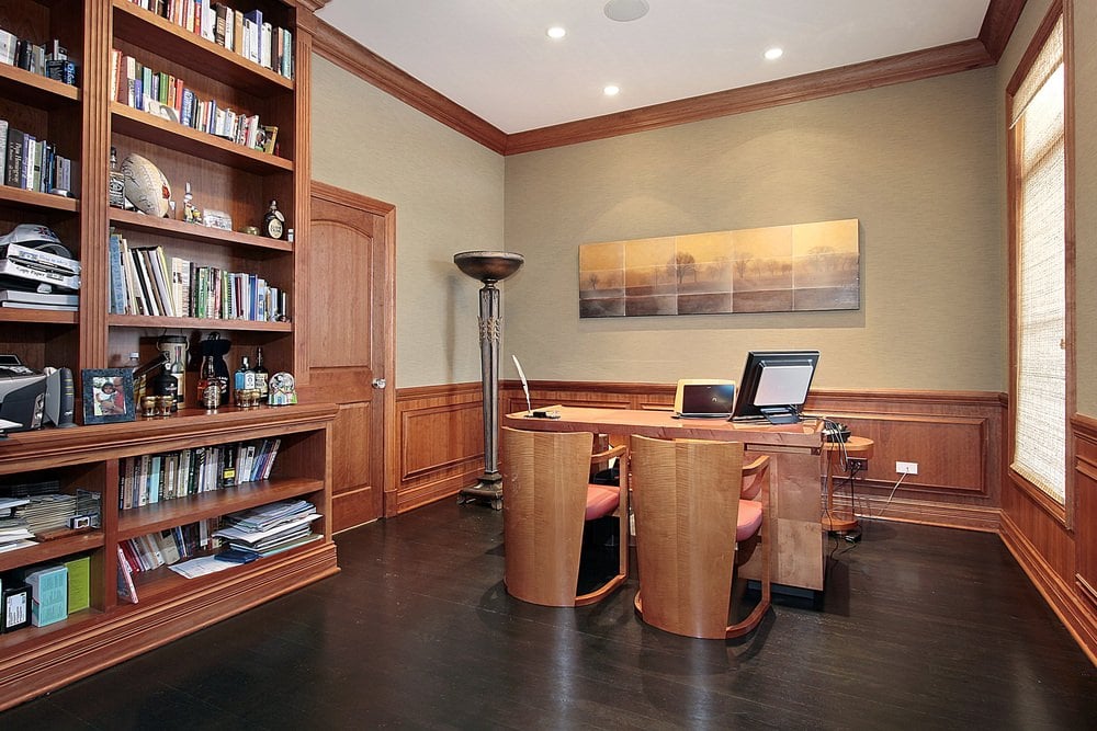 一个经典的家庭办公室，装饰有多层帆布墙面艺术，安装在木制护壁板上。它有一张木制的办公桌和配有红色靠垫的椅子。