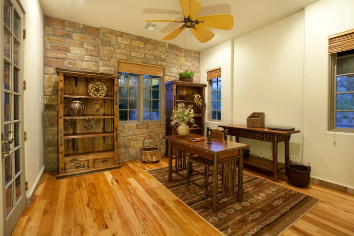 乡村风格的家庭办公室以一对展示柜和一张木桌为特色。它有一面石砖墙和天然硬木地板，上面有棕色图案的地毯。