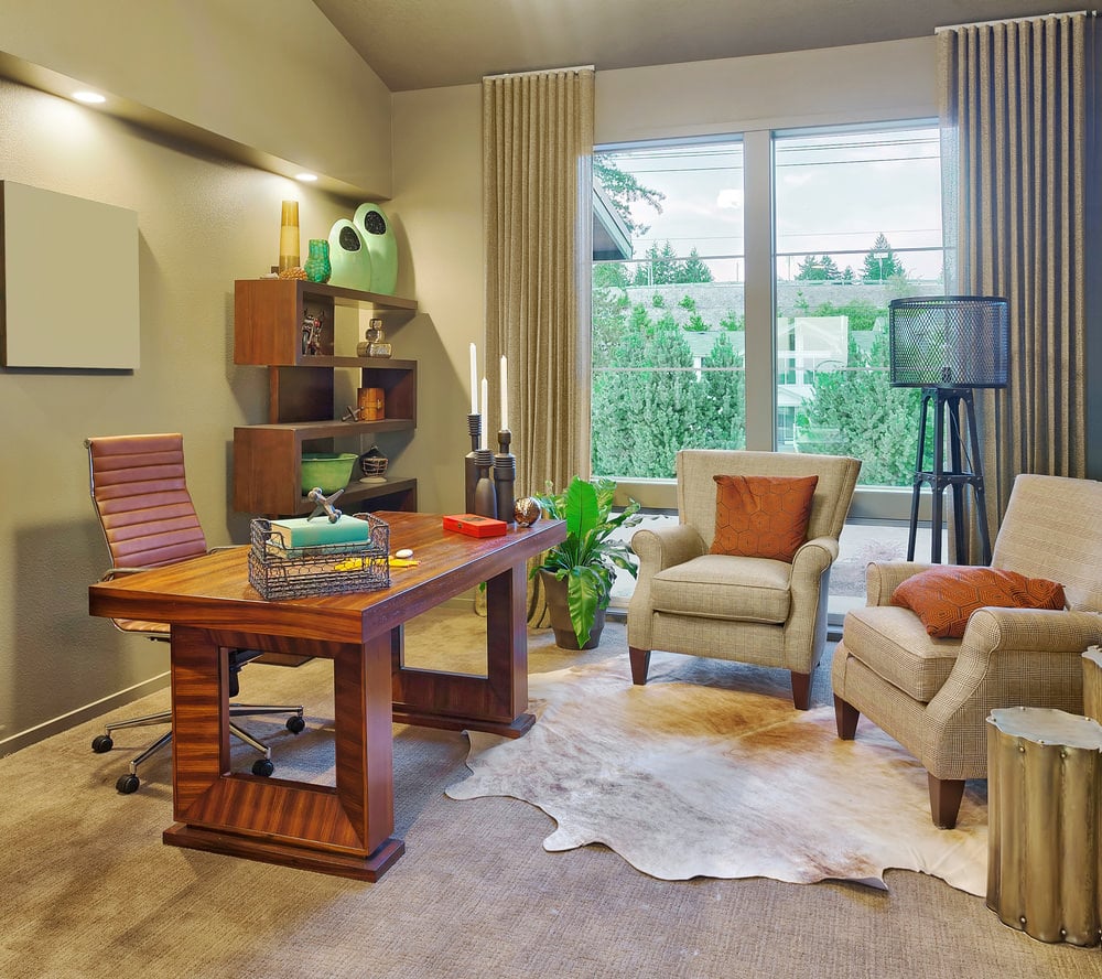 一个中等大小的家庭办公室，有一张时尚的办公桌和优雅的椅子，放在地毯地板上，上面有迷人的地毯。