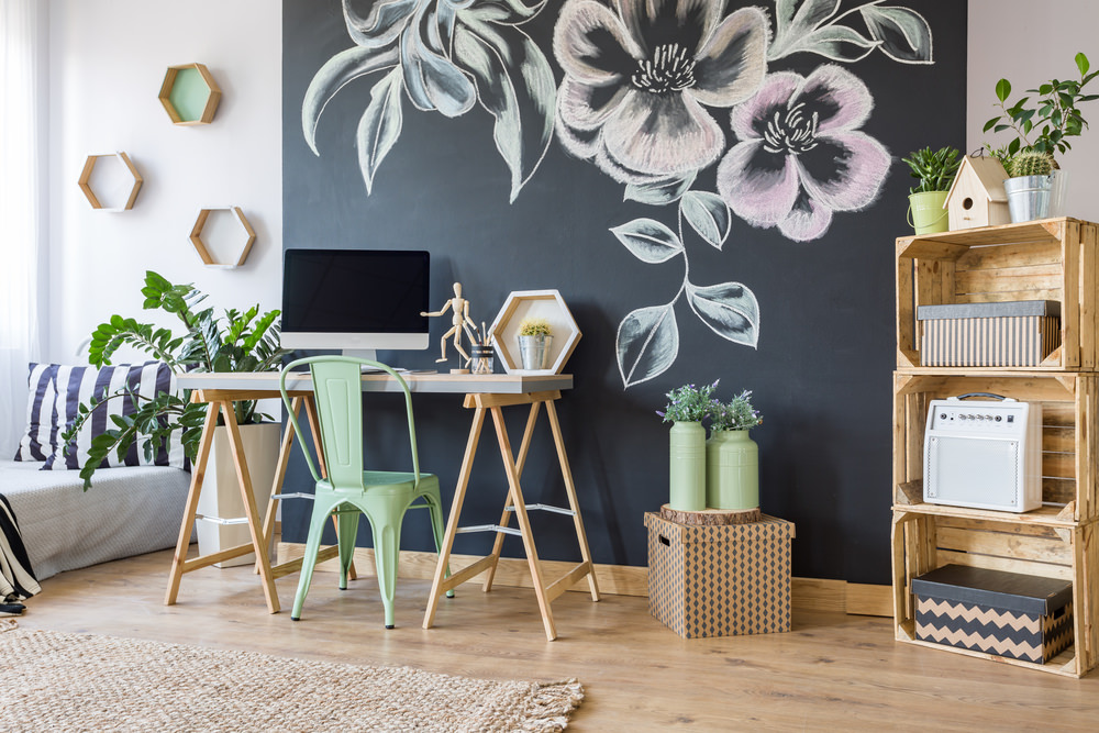 新鲜的家庭办公室设计，黑色的花墙艺术和六角形木架安装在白色的墙壁上。它有一张浅色的木头桌子和绿色的椅子，还有乡村风格的开放式架子，上面摆满了储物箱。
