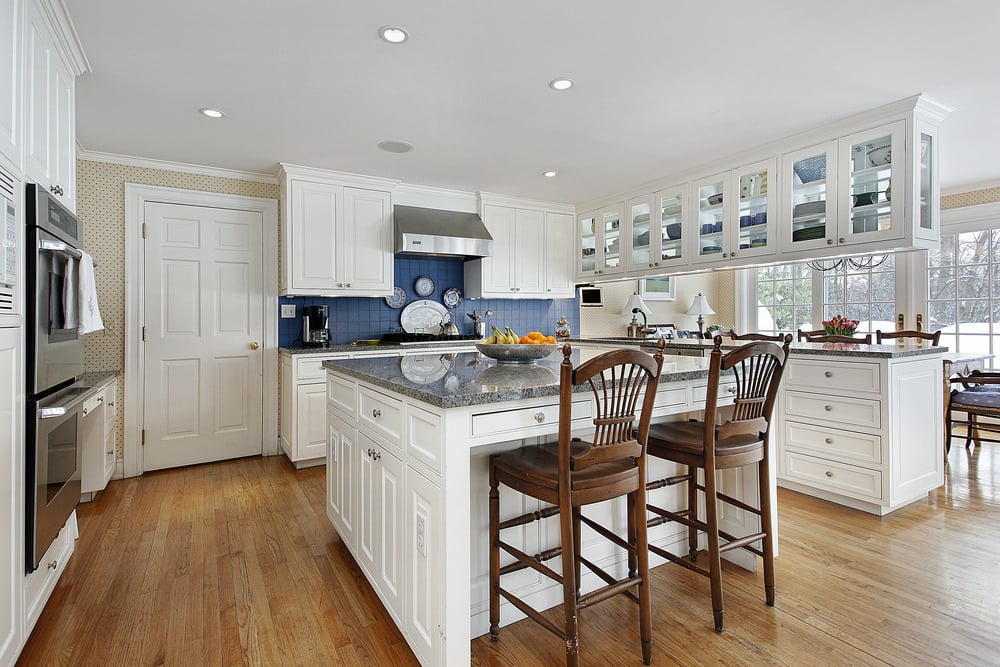 白色厨房设有一个大的中央岛和半岛组合。硬木地板、白色橱柜和天花板搭配在一起很好看。