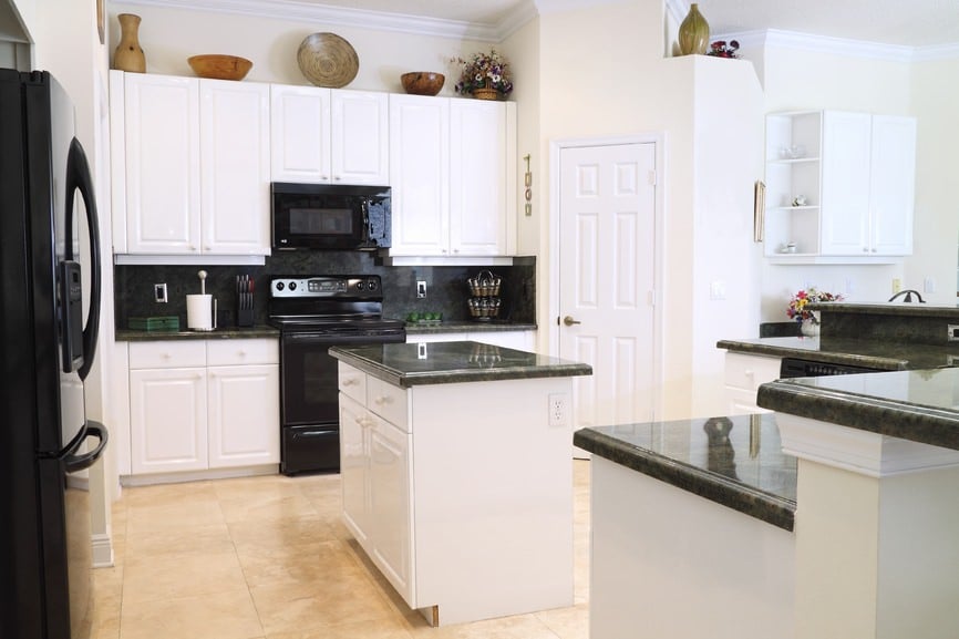 白色厨房配有瓷砖地板，黑色柜台和电器，以及一个小的中心岛和半岛。