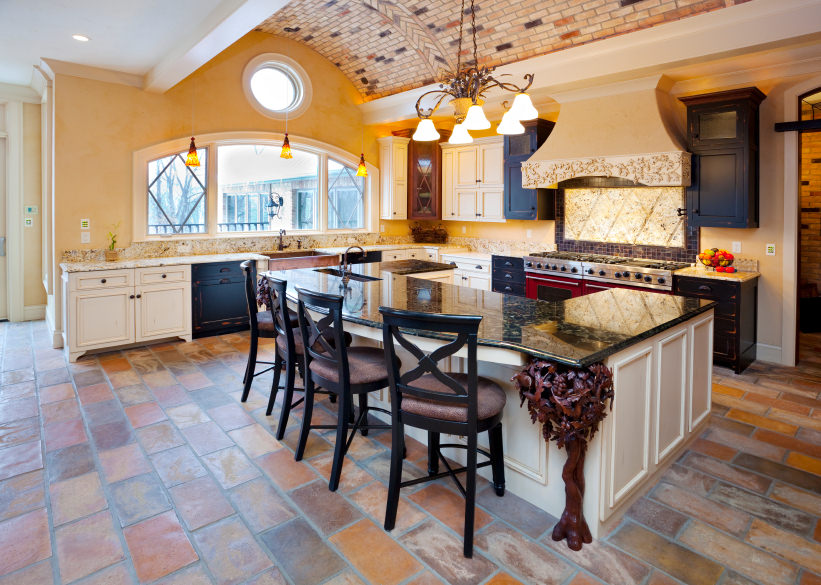 地中海风格的厨房设有一个由砖制成的凹形天花板，赤陶砖地板和大量的自然光线从一个大的主窗和较小的舷窗。u形的厨房岛包括早餐吧。