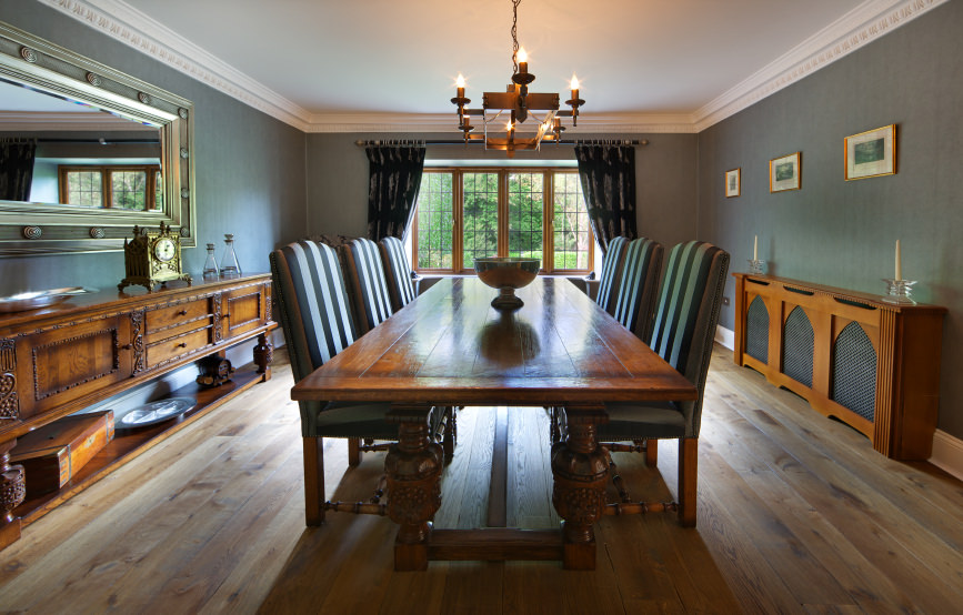 正式的餐厅，木制餐桌周围的条纹椅子之间的木制控制台桌子。它的玻璃窗上覆盖着黑色的窗帘。