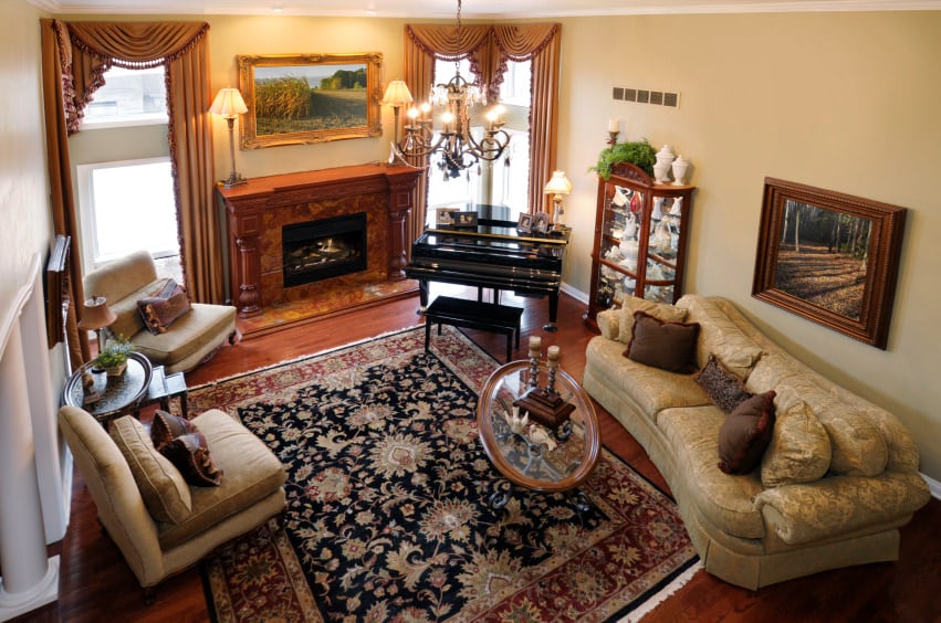 这间正式的客厅设有一座优雅的壁炉。壁炉旁边是一架黑色的钢琴，看起来美极了。红色的硬木地板上铺着漂亮的地毯，上面有一盏华丽的枝形吊灯。