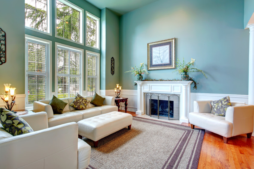优雅正式的客厅设有白色沙发套，两个巨大的俱乐部椅和配套的软脚凳。该空间还包括一座燃木壁炉、硬木地板和一块大面积地毯。墙壁和高高的天花板是蓝色/绿色的柔和颜色，大窗户让充足的自然光进入。