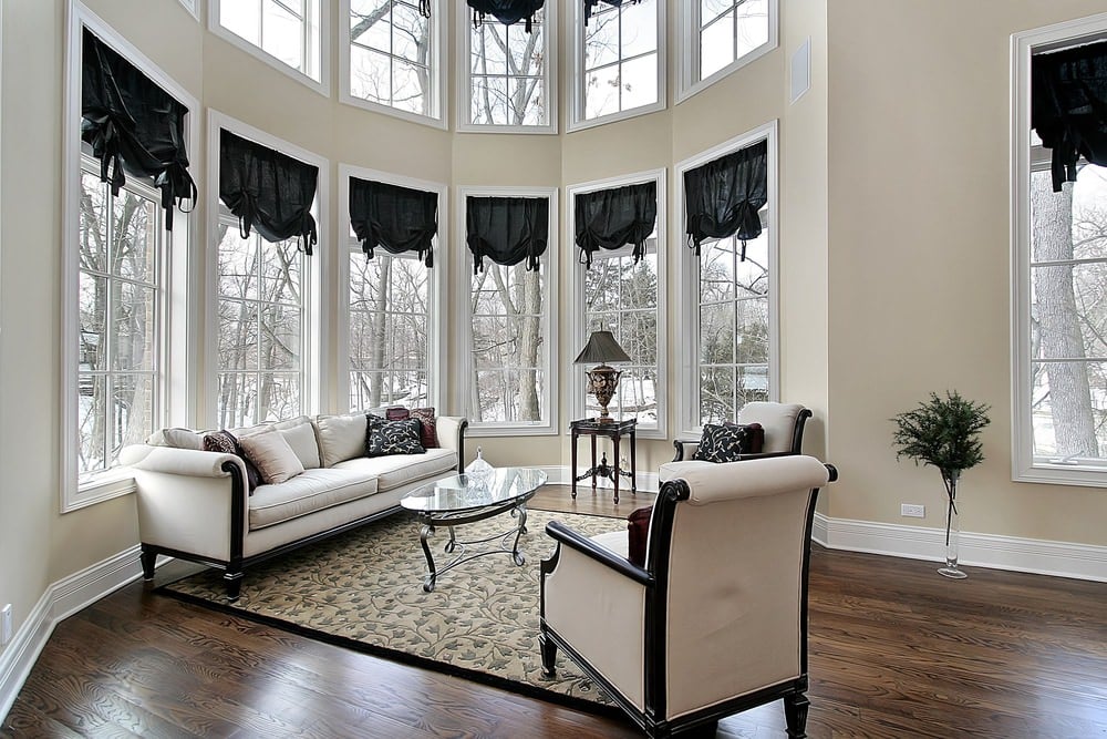 优雅的客厅设有硬木地板，上面有地毯。这套沙发和落地窗配上漂亮的窗帘看起来很漂亮。高高的天花板使房子看起来美极了。
