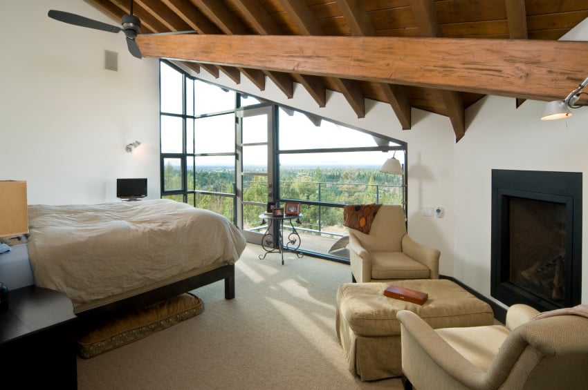 这间主卧有一张舒适的床，一座带休息区的壁炉，白色的墙壁和地毯地板，天花板上有外露的横梁。