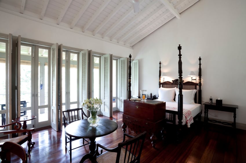 这间卧室提供一张精致的床，铺着红色的硬木地板，周围是白色的墙壁和天花板。