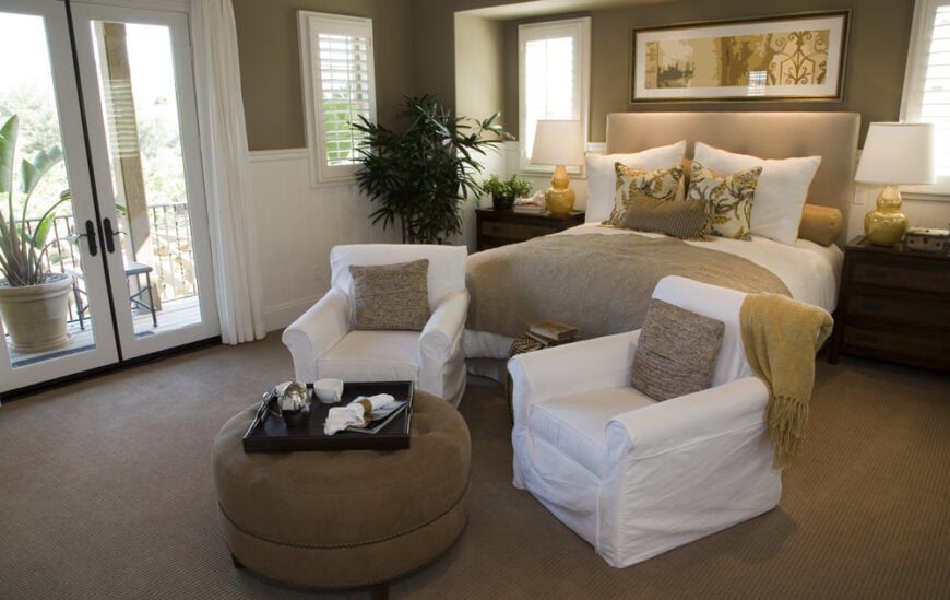 一间主卧室，有一张漂亮的床和一个棕色地毯地板上的休息区。房间还设有棕色墙壁和白色遮阳。