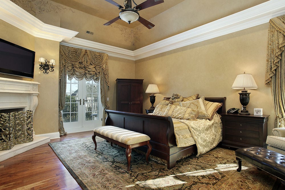 优雅的主卧室展示了深色木质家具，与白色壁炉和覆盖着华丽窗帘的法式门形成对比。
