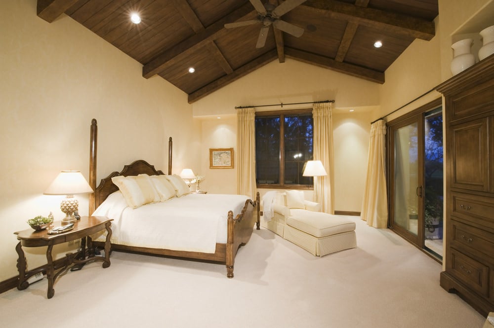 明亮的主卧室，白色地毯地板和一张大床下的拱形天花板与横梁。