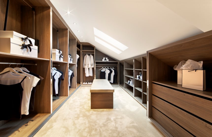 一个别致的步入式衣帽间功能优雅木橱柜,地板,地毯,天花板天窗和隐藏式照明。