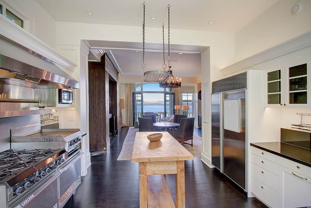 农舍厨房与不锈钢器具和一个空的悬挂potrack上方的木桌厨房岛。