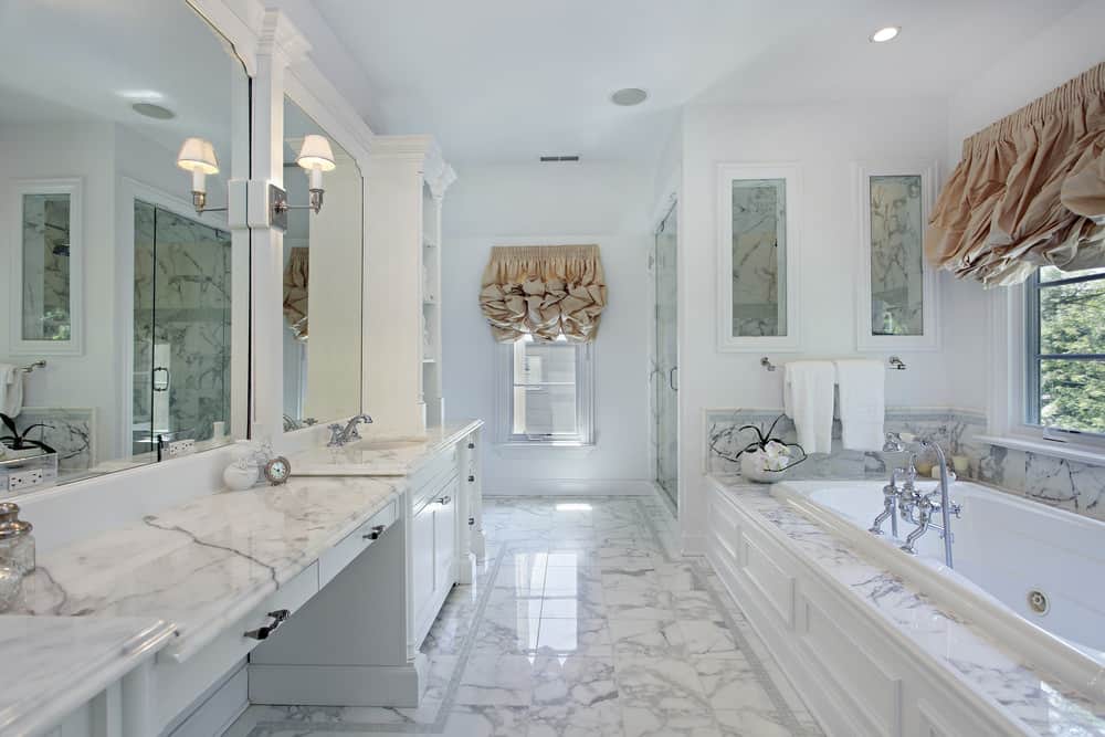 白色主浴室拥有大理石瓷砖地板和大理石水槽台面。靠近窗户的地方有一个可放下的浴缸，角落里还有一个步入式淋浴间。