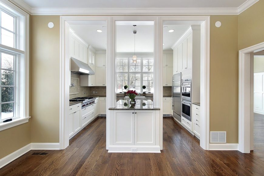 大而时尚的u型厨房，设有硬木地板和白色橱柜和柜台，由嵌入式和吊灯照明。