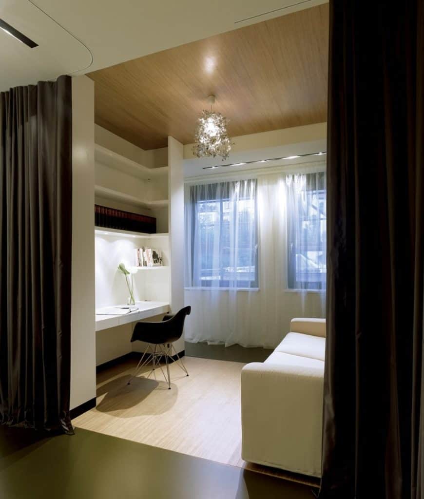 当代家庭办公室，内置书架和办公桌，配上黑色的办公椅，上面是柳条地毯。它包括一个白色舒适的沙发和一个独特的吊灯挂在木制天花板上。