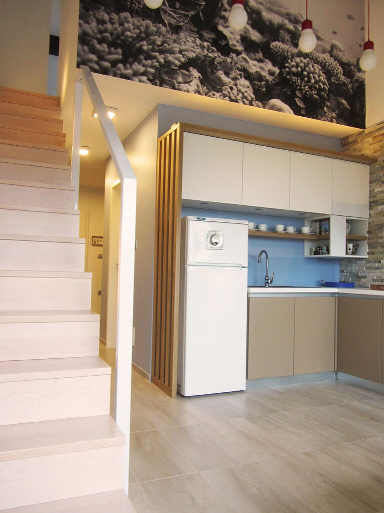 白色橱柜和冰箱上方是一个小厨房，装饰着黑白相间的珊瑚礁墙壁艺术。它有一个固定在浅蓝色后挡板上的木制浮动搁板，与下部的棕色橱柜相辅相成。