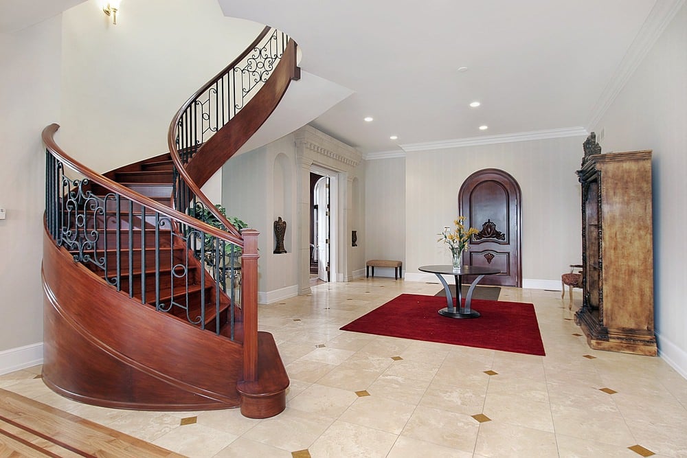 这个白色的门厅采用了一套时尚的瓷砖地板，上面是红色的地毯，还有一个质朴的楼梯。
