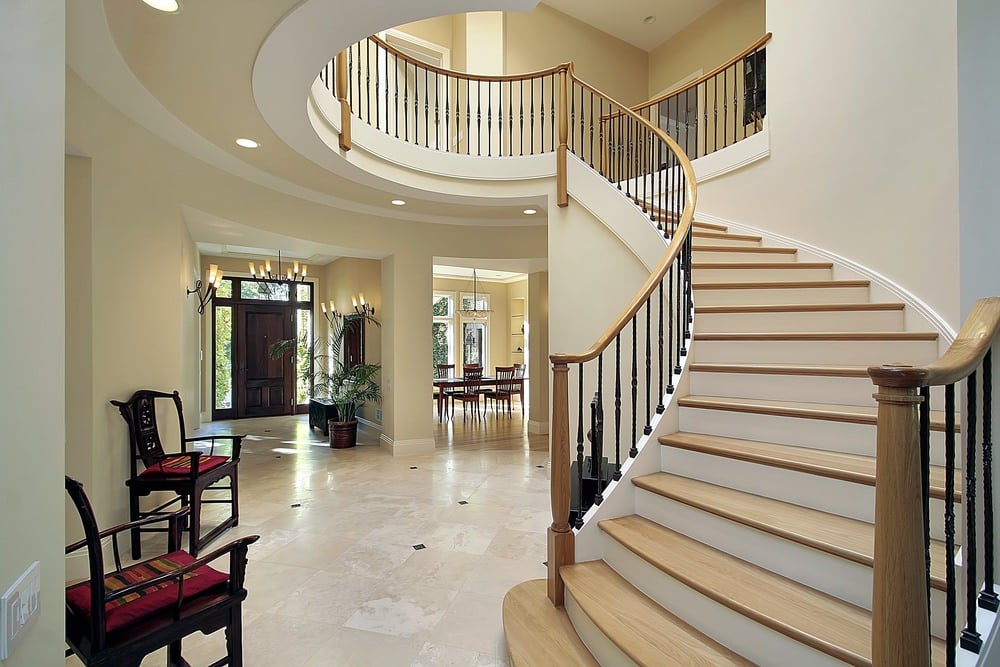 这个白色的门厅设有华丽的楼梯和时尚的地板，以及几把优雅的椅子。