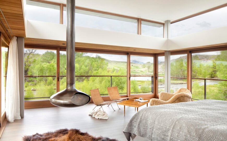 通风的主卧室周围环绕着玻璃镶板墙，拥有一个现代的悬挂壁炉和一个小休息区。